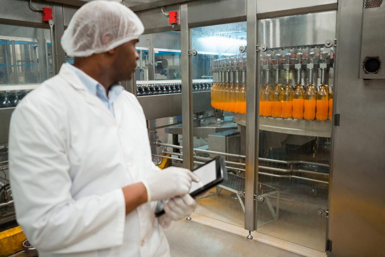 Male worker holding digital tablet while inspecting juice bottles in factory